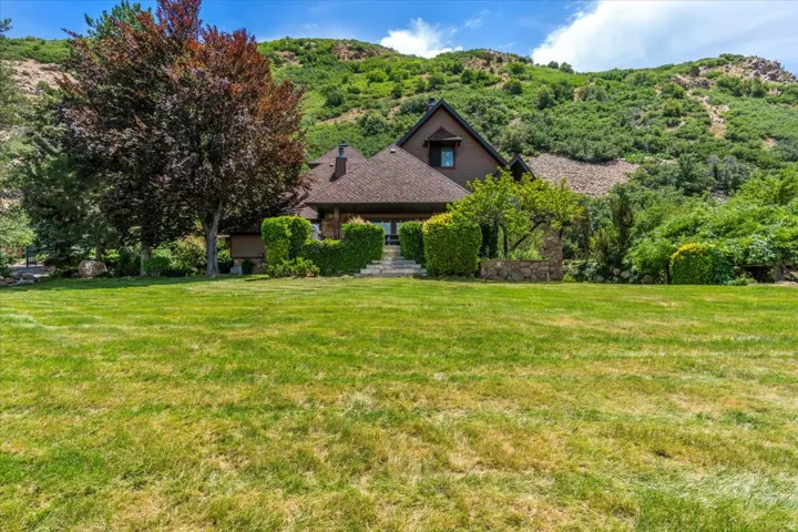Expansive front lawn with a backdrop of a sloped, tree-covered hillside