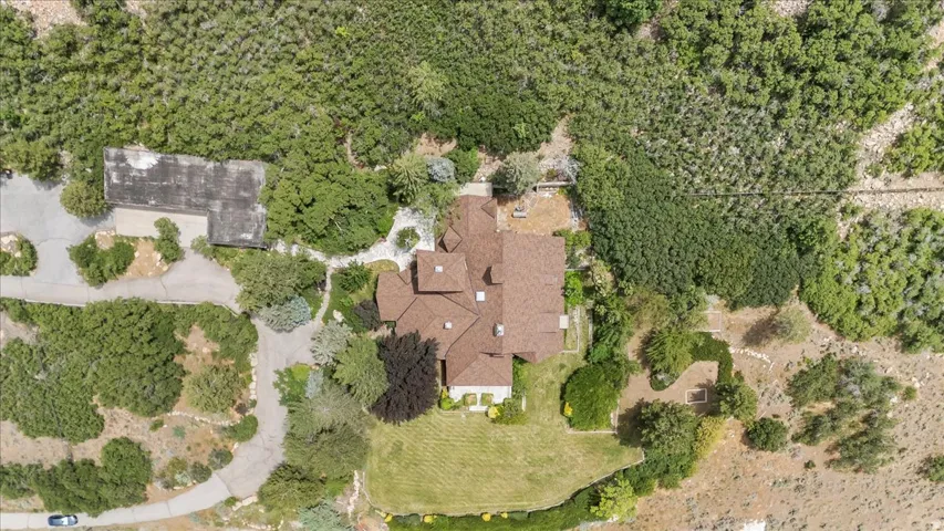 Expansive property featuring a multi-gabled brown shingle roof, paved driveways, a manicured lawn area, and surrounding natural landscaping
