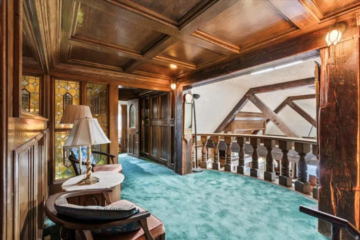 Wood-paneled hallway featuring a coffered ceiling and ornate balustrade overlooking architectural beams