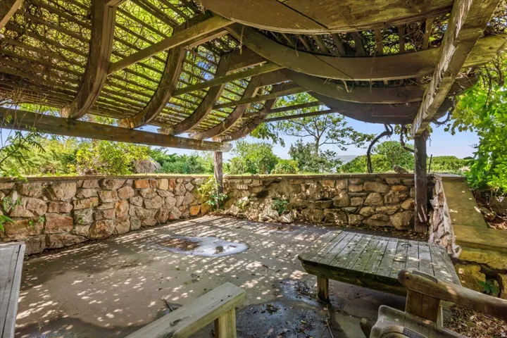 Outdoor patio featuring a curved wood pergola with mature vine coverage, a stone retaining wall, and a concrete patio surface