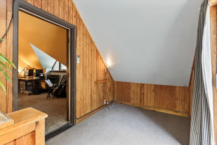 Carpeted attic space featuring wood paneling, sloped ceilings, and recessed lighting