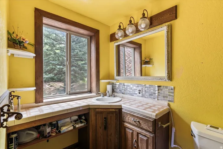 Bathroom featuring a corner vanity with a drop-in sink, tiled countertop, and wood cabinetry