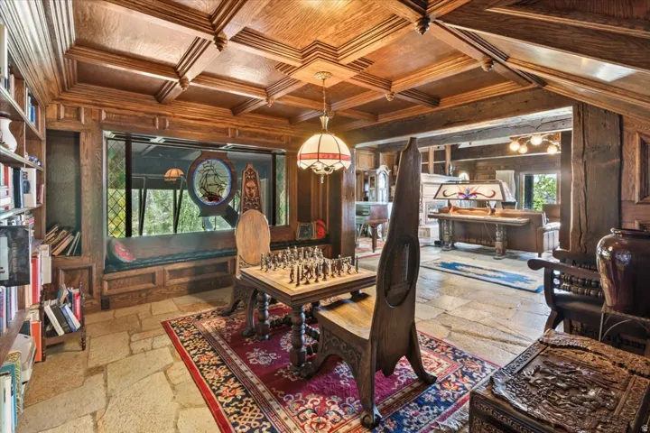 Spacious room featuring extensive wood coffered ceilings, stone tile flooring, built-in shelving, a window seat, and a decorative stained glass insert