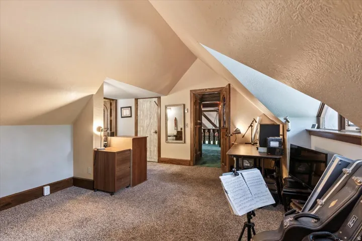 Carpeted loft area featuring an angled ceiling, dark wood trim, and a built-in window with wood-frame