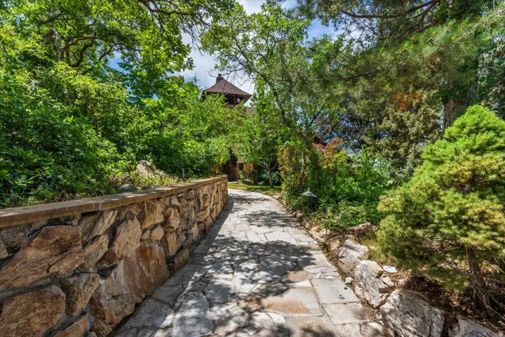 Stone pathway with a natural stone retaining wall, surrounded by mature trees and lush landscaping