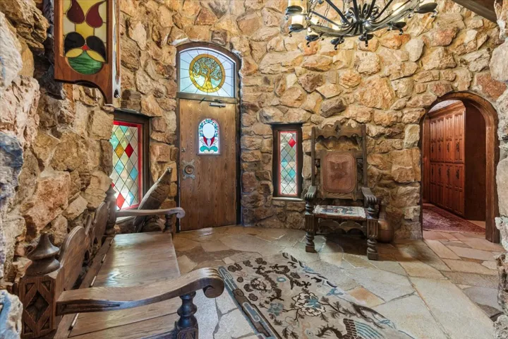 Stone-clad entryway featuring flagstone flooring, a wooden entry door with stained glass, additional stained glass windows, and a wrought iron chandelier