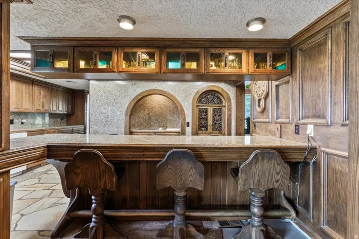 Custom wood-paneled bar featuring a stone countertop and integrated glass-front cabinetry