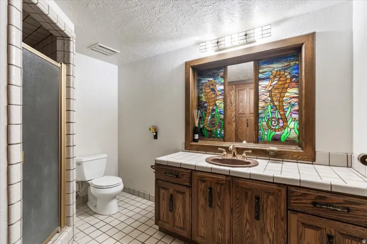 Custom stained-glass mirror with wood frame, vanity with tile countertop, and wood-finish cabinetry