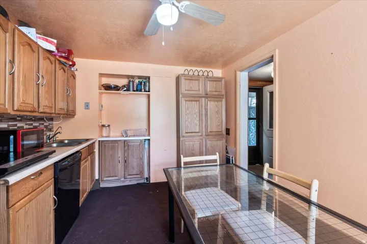 Kitchen featuring wood-finish cabinetry, black appliances, a tile backsplash, and a ceiling fan with light fixture