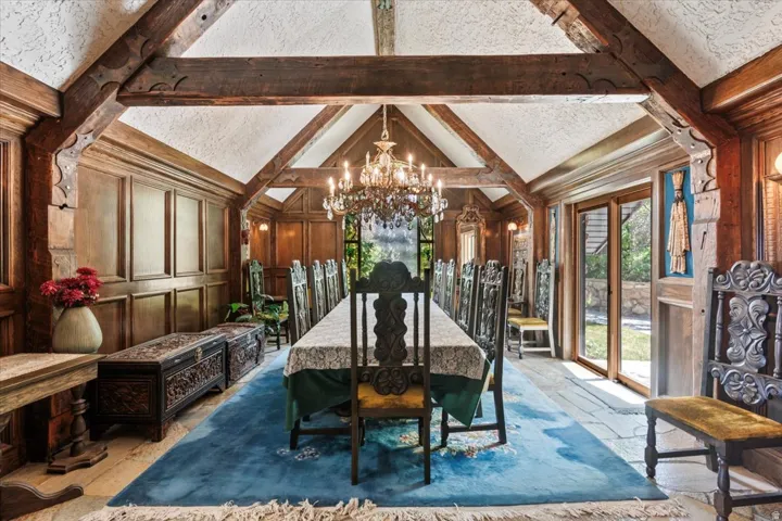 Formal dining area featuring exposed wood beams, wood paneling, a crystal chandelier, and stone flooring