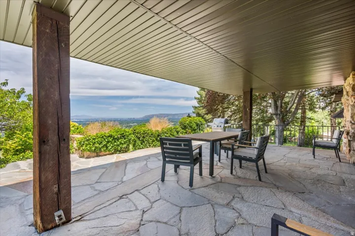 Expansive covered patio featuring flagstone flooring, a large wood support beam, and a stone exterior wall