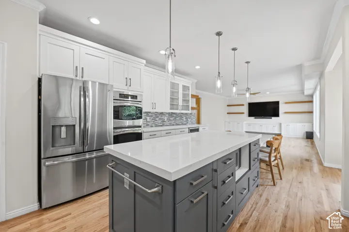 Gourmet kitchen with stainless steel appliances, white shaker cabinetry, and a large central island featuring a light-toned countertop