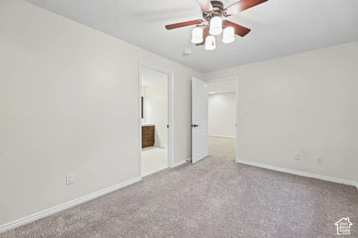 Neutral wall paint, textured carpet flooring, ceiling fan with integrated lighting, white trim, and a wood-finish vanity with a white countertop