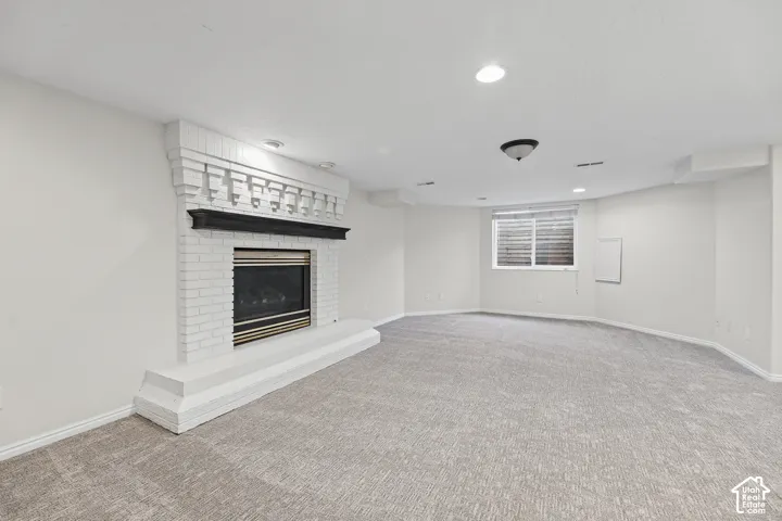 White brick fireplace with dark wood mantel, recessed lighting, ceiling-mounted light fixture, light-colored carpeting, and a window with blinds
