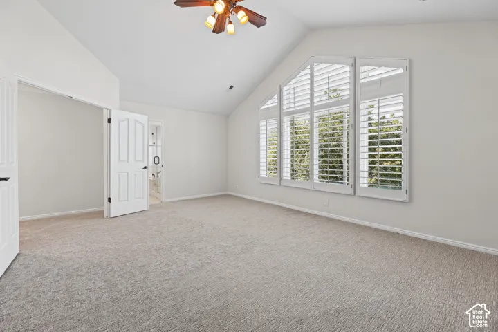 Vaulted ceiling with a wood-finish ceiling fan, expansive window with plantation shutters, light gray carpet, and white paneled doors