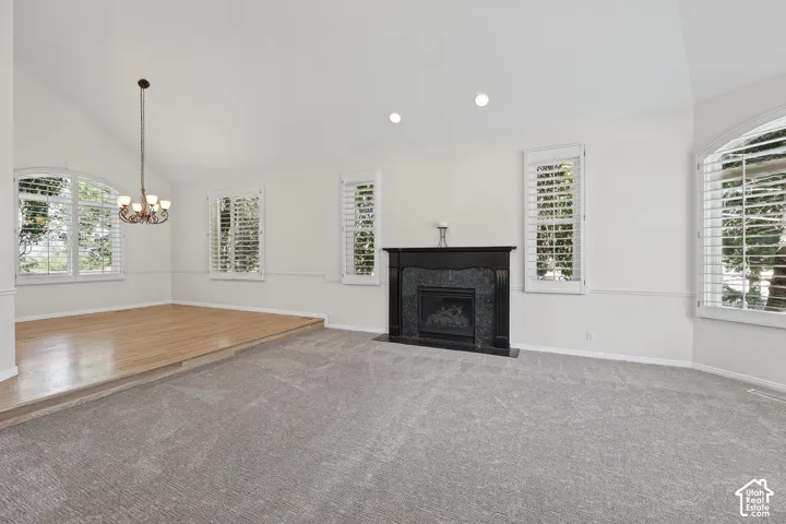 Vaulted ceiling, recessed lighting, fireplace with stone surround, plantation shutters, and wood-finish flooring