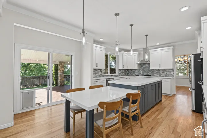 Kitchen featuring white cabinetry, a center island with seating, a tile backsplash, and light wood-finish flooring