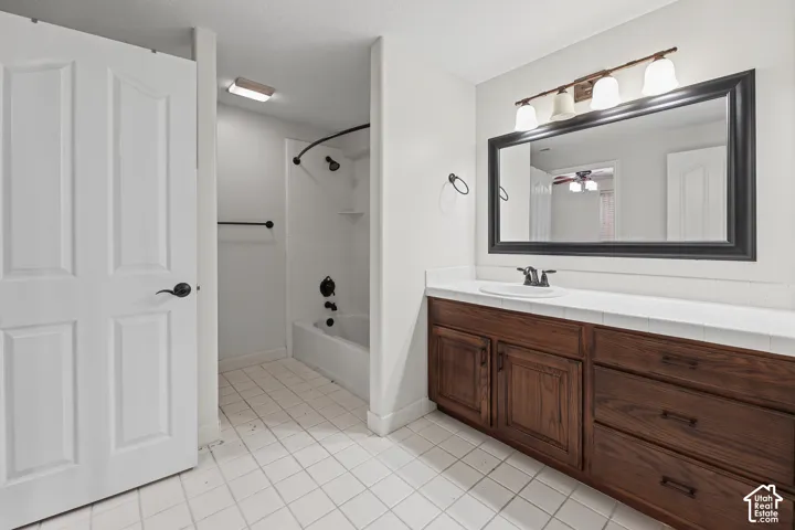 White tile flooring, wood-finish vanity with countertop, framed mirror, and a built-in tub with shower