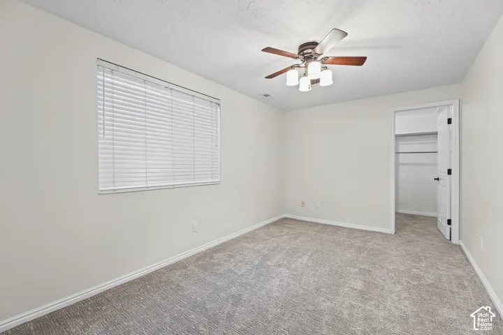 Neutral wall paint, textured carpeting, window with blinds, ceiling fan with light fixture, and closet with shelving