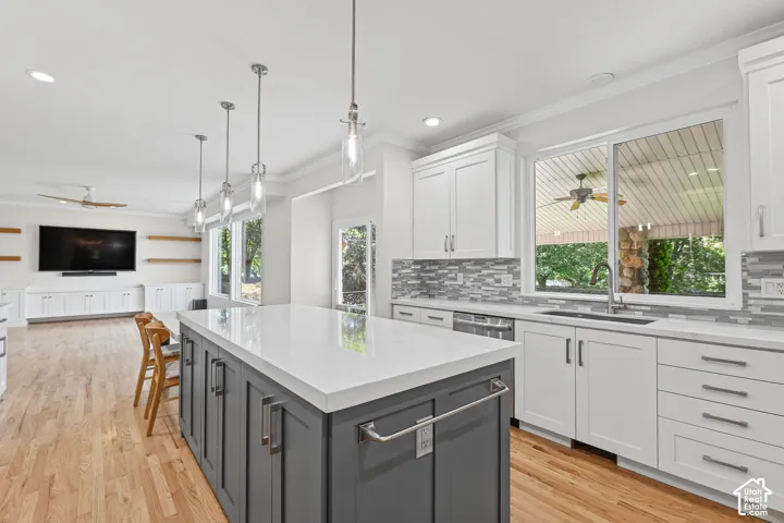 Spacious kitchen with a central island featuring a light-toned countertop, white cabinetry with modern hardware, and a tile backsplash