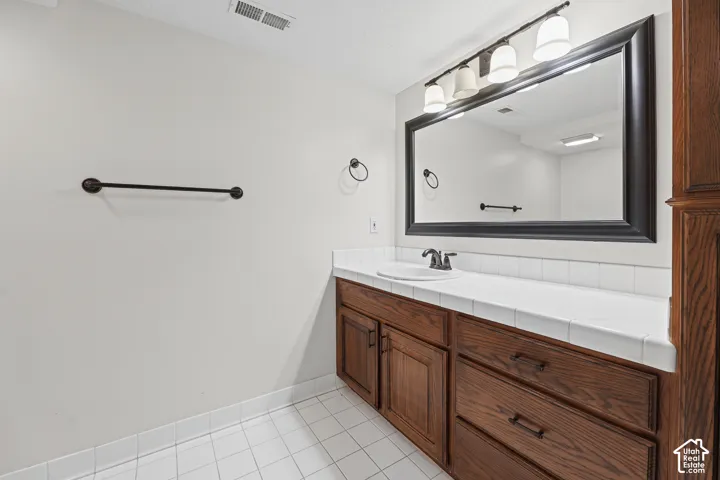 Built-in wood-finish vanity with an integrated sink, white tiled countertop, dark bronze fixtures, and a large framed mirror with overhead lighting