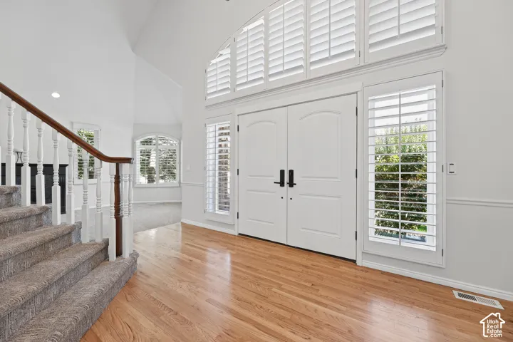 Double entry doors with transom windows, wood-finish flooring, custom plantation shutters, and a carpeted staircase with a wood handrail
