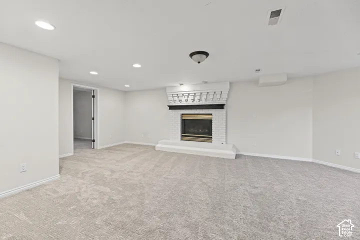 Spacious carpeted room featuring a white brick fireplace with a black mantel, recessed lighting, and a neutral color palette