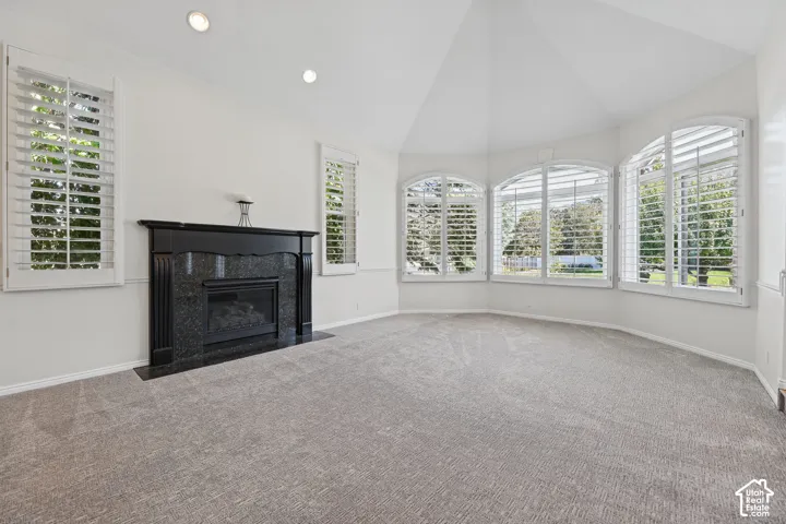 Recessed lighting illuminates a spacious room featuring a black granite-clad fireplace, arched windows with plantation shutters, and light-colored carpeting