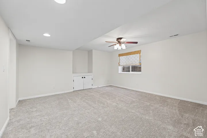 Spacious room featuring neutral carpeting, a ceiling fan, recessed lighting, a window with a valance, and built-in cabinetry