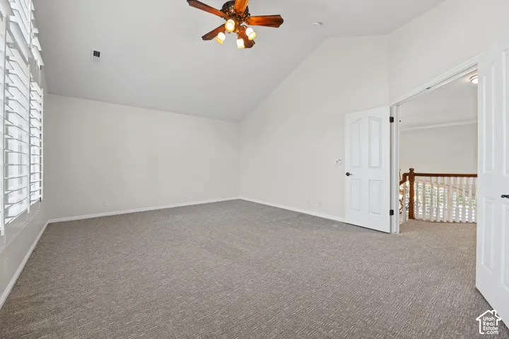 Vaulted ceiling, ceiling fan with integrated lighting, plantation shutters, grey carpeting, and white paneled doors