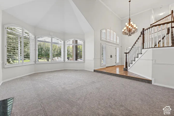 Vaulted ceilings, arched windows with plantation shutters, wood-finish flooring at entry, grand staircase with wood railing, and an ornate chandelier