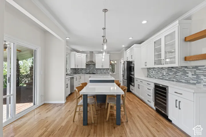 Kitchen featuring wood-finish flooring, white cabinetry, a central island with countertop seating, stainless steel appliances, and a tiled backsplash