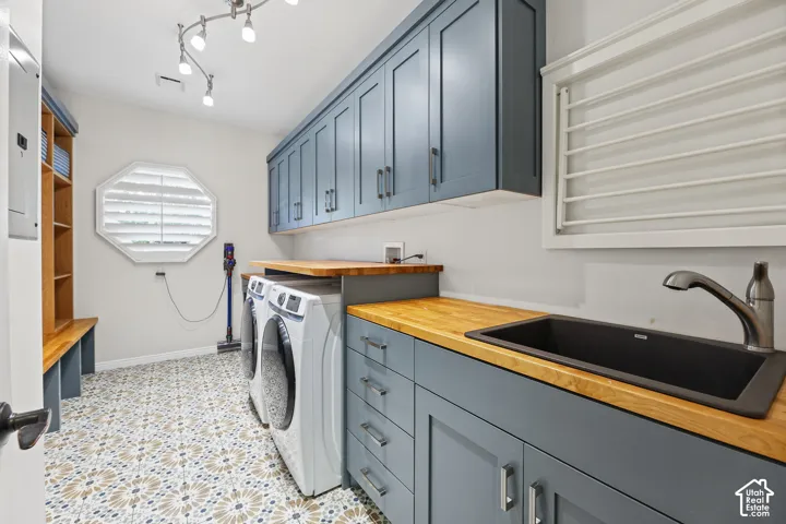 Laundry room featuring patterned floor tiles, light blue cabinetry, butcher block countertops, a utility sink with a gooseneck faucet, and an octagonal window with plantation shutters