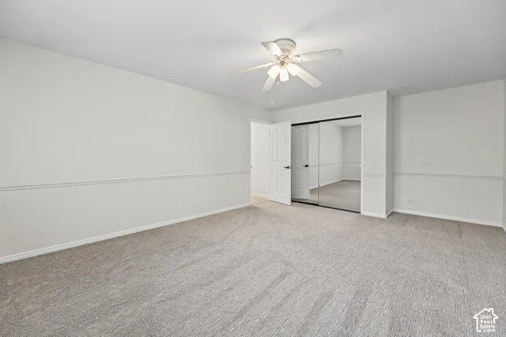 Neutral wall finishes, textured carpeting, mirrored closet doors, ceiling fan, and white paneled door
