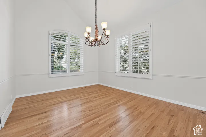 Vaulted ceiling with a decorative chandelier, hardwood flooring, and white plantation shutters