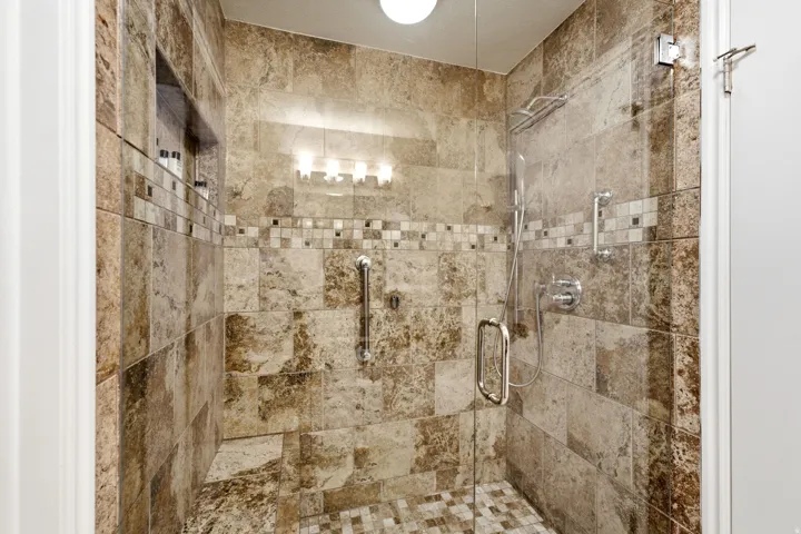 Tiled shower enclosure featuring a glass door, built-in shelving niche, mosaic accent banding, rain showerhead, and a handheld shower fixture