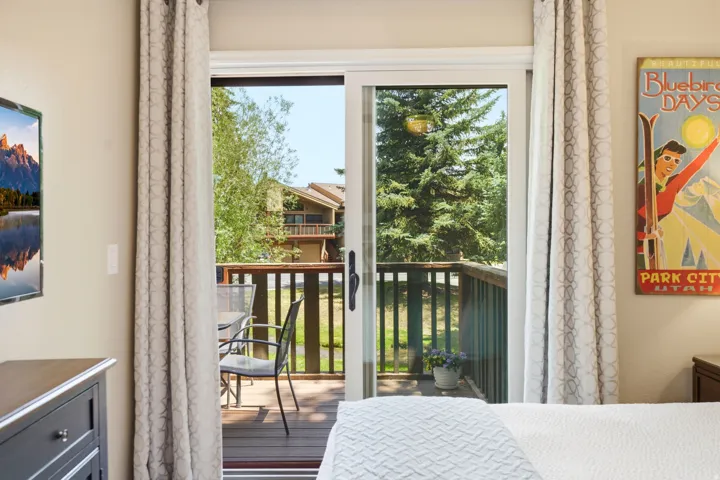 Sliding glass door opening to a private deck with natural wood railings, overlooking mature evergreen trees