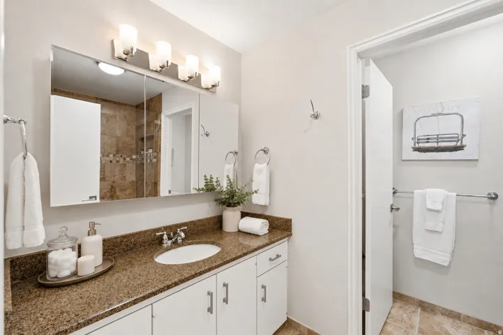 Bathroom featuring a vanity with a brown granite countertop, an integrated sink, and white cabinetry