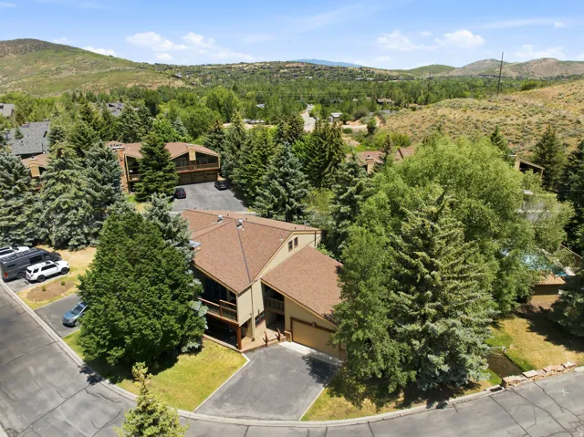 Sloping hillside property featuring a multi-level structure with a brown shingle roof, integrated garage, and a private balcony