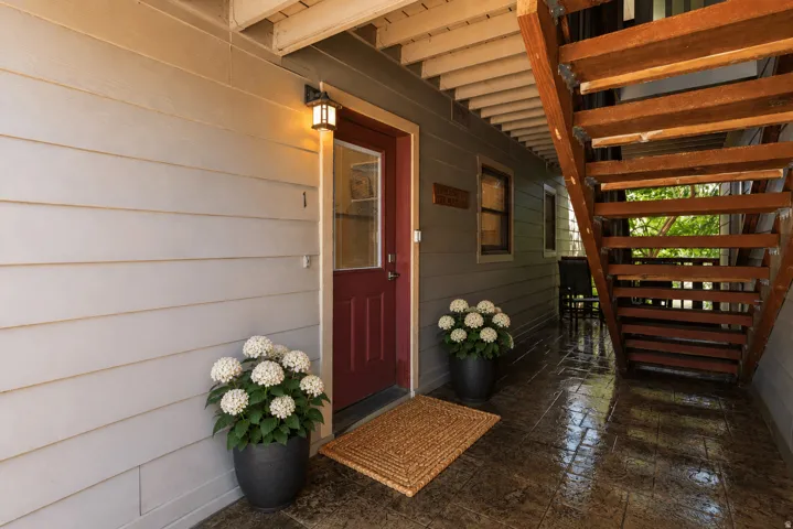 Covered entry featuring a red-paneled door, exterior wall lantern, and wood-finish stairs