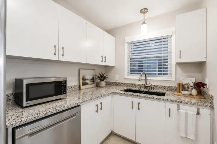 Kitchen featuring white cabinetry with silver hardware, speckled countertops, and a double basin sink with a gooseneck faucet