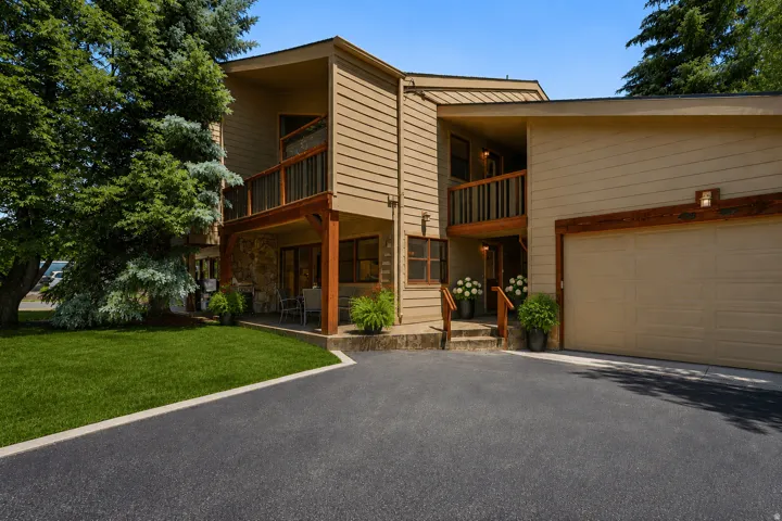 Exterior featuring horizontal siding and stone accents, a two-car garage, upper and lower balconies with wood railings, a paved driveway, and established landscaping