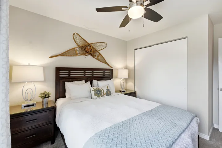 Spacious room featuring a dark wood-finish headboard, dual nightstands with contemporary lamps, a ceiling fan with integrated lighting, and a closet with bi-fold doors