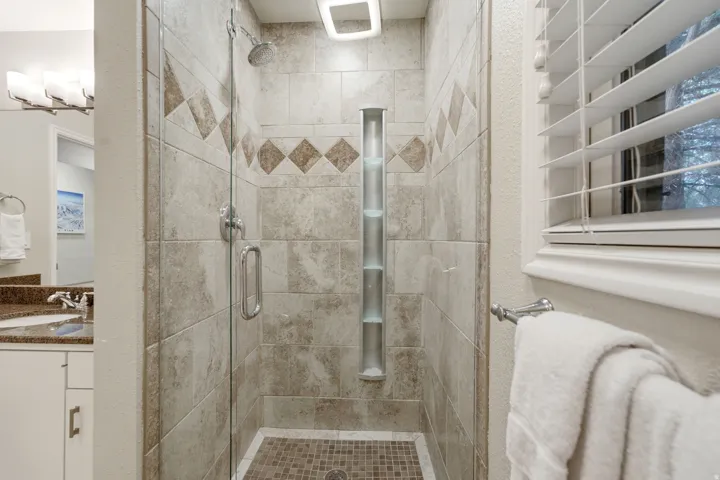 Glass-enclosed shower featuring large format wall tiles with a decorative accent band, a built-in vertical storage niche, and a mosaic tile floor