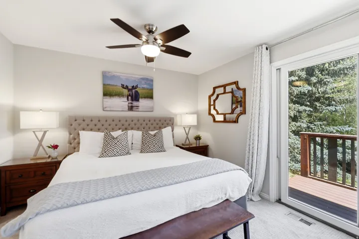 Carpeted bedroom featuring a tufted headboard, ceiling fan with integrated lighting, and a sliding glass door opening to a private deck