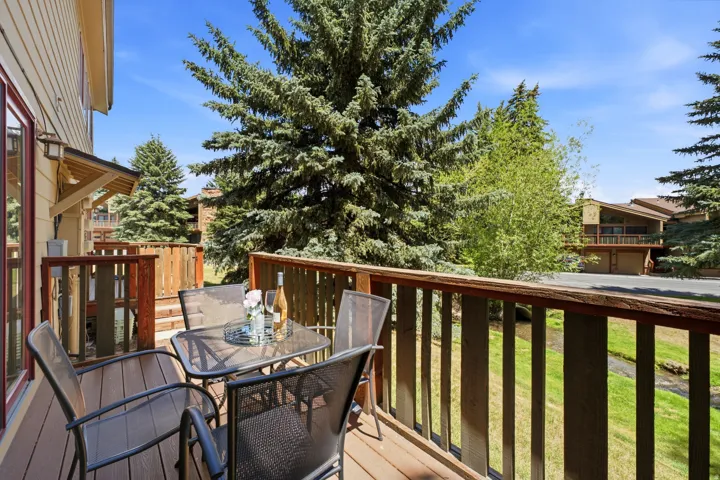 Private outdoor deck featuring wood-finish decking and railing, with a clear view of mature evergreen trees and a naturally landscaped area