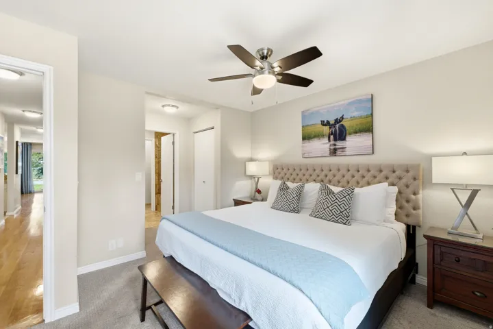 Carpeted bedroom featuring a tufted headboard, ceiling fan with light, and light neutral wall tones