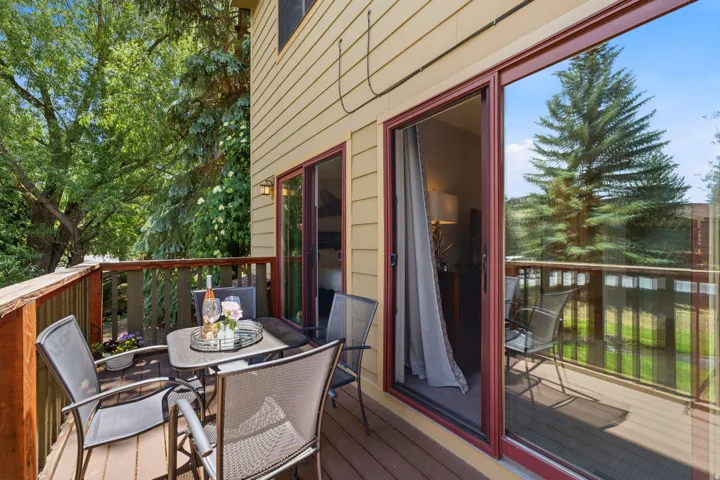 Outdoor wood-finish deck featuring a wood railing and two sliding glass doors with red trim