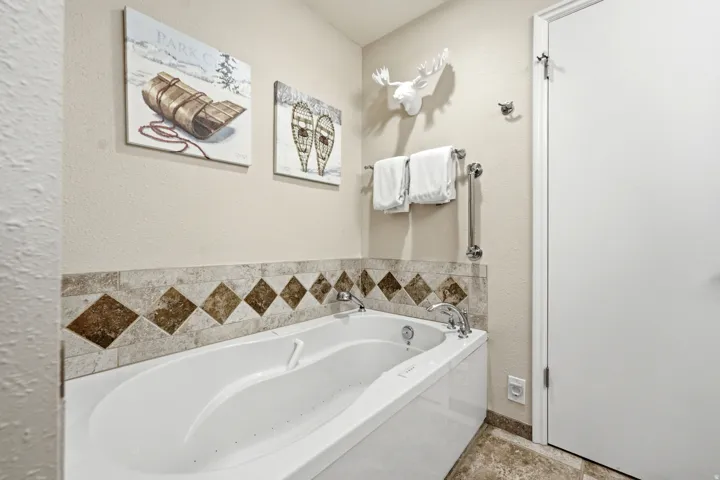 Jetted soaking tub with a tiled surround featuring diamond-patterned accents, chrome fixtures, and a neutral wall finish