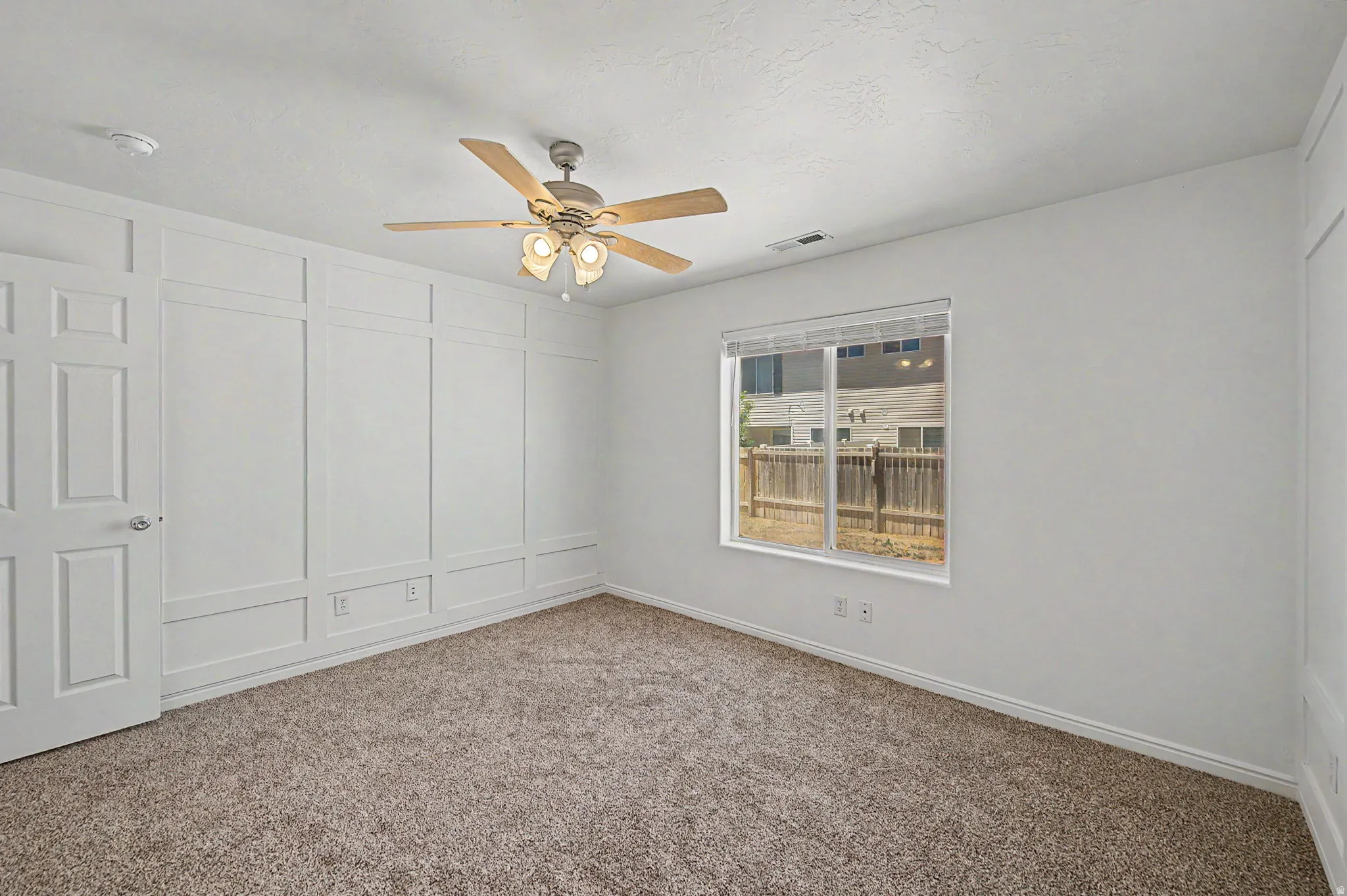 Neutral-toned carpet flooring and white walls, featuring a window with horizontal blinds and a wooden fence visible outside